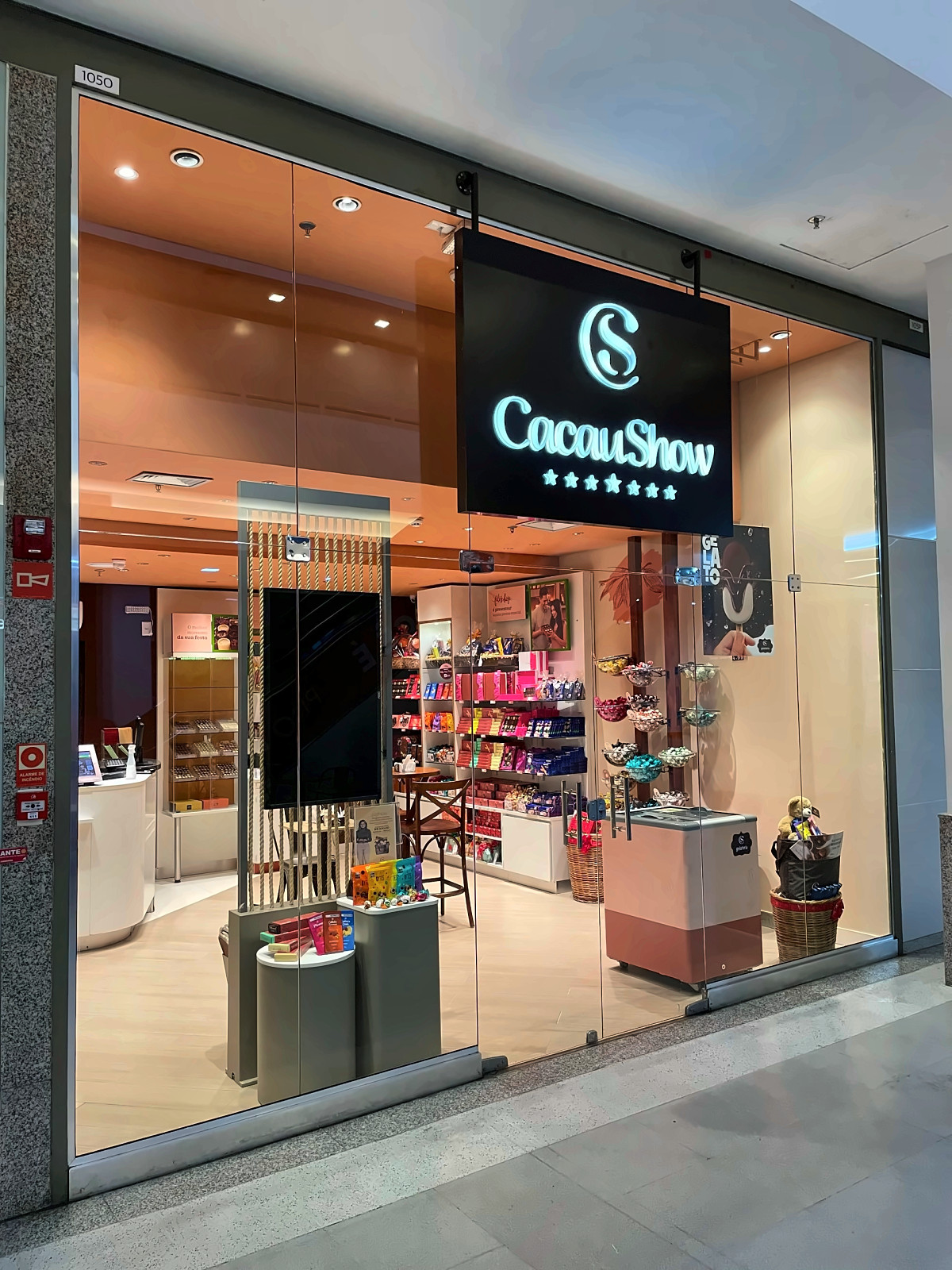 Fachada de loja Cacau Show em shopping, com vitrine de vidro e letreiro iluminado