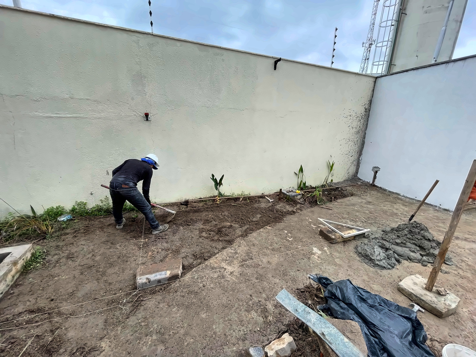 Profissional da Enobras preparando o terreno junto ao muro para o piso externo
